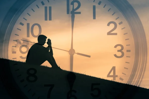 eine große Uhr im Hintergrund, ein Mensch sitzt davor, schattiges Ambiente